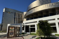 The exterior of a modern institutional building with distinctive architectural features and an outdoor art element.
The building has a contemporary design with a curved facade clad in light-colored stone or textured panels.
