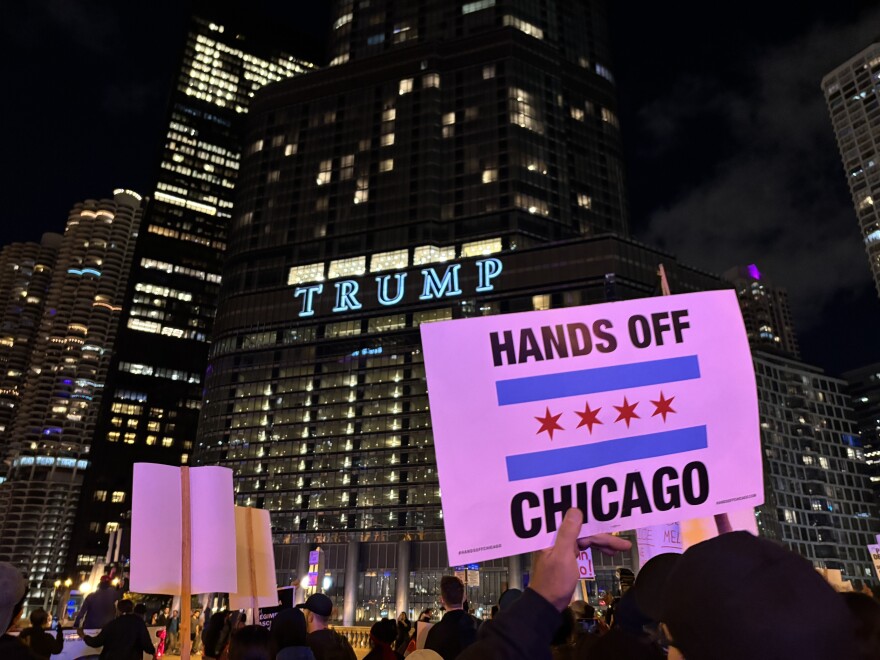 A sign is held above a person's head outside Trump Tower at night reading: Hands off Chicago, with the city's distinctive four star flag in the middle.