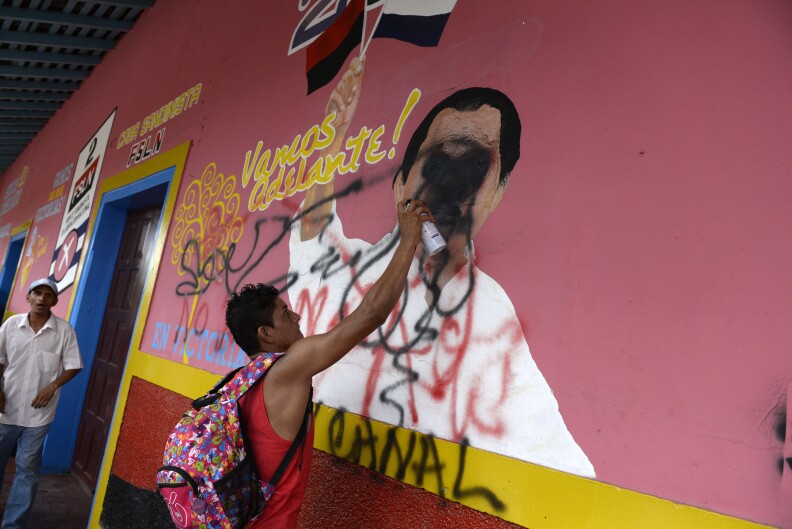 A peasant makes a graffiti on a mural of Nicaraguan Presidnet Daniel Ortega during a protest against the construction of an inter-oceanic canal in Juigalpa, Nicaragua on June 13, 2015. Nicaragua and Chinese company HKND Group last year launched construction of an ambitious $50 billion rival to the Panama canal that could handle even larger ships. The canal, which is set to be completed within five years, threatens to displace a small village of the Rama ethnic group and to invade the Indio Maiz reserve, according to environmentalists. AFP PHOTO / STR        (Photo credit should read STR/AFP/Getty Images)
