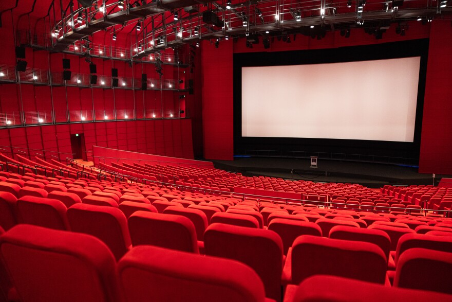 A large movie theater with rows of red seats and a large screen.