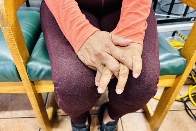 A person's hands with fingers interlaced on their lap.