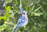 A hand crafted ceramic ornament depicting a blue jay hangs in a tree. 
