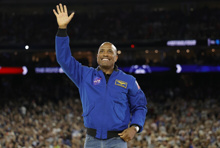 A Black man in a blue jacket with a NASA emblem on the front waves to the crowd inside Houston's NRG Stadium at the NCAA Men's Basketball National Championship on Monday, April 3, 2022.
