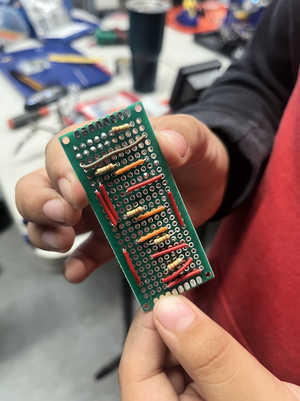 A closeup of a small circuit board with red and orange wires.