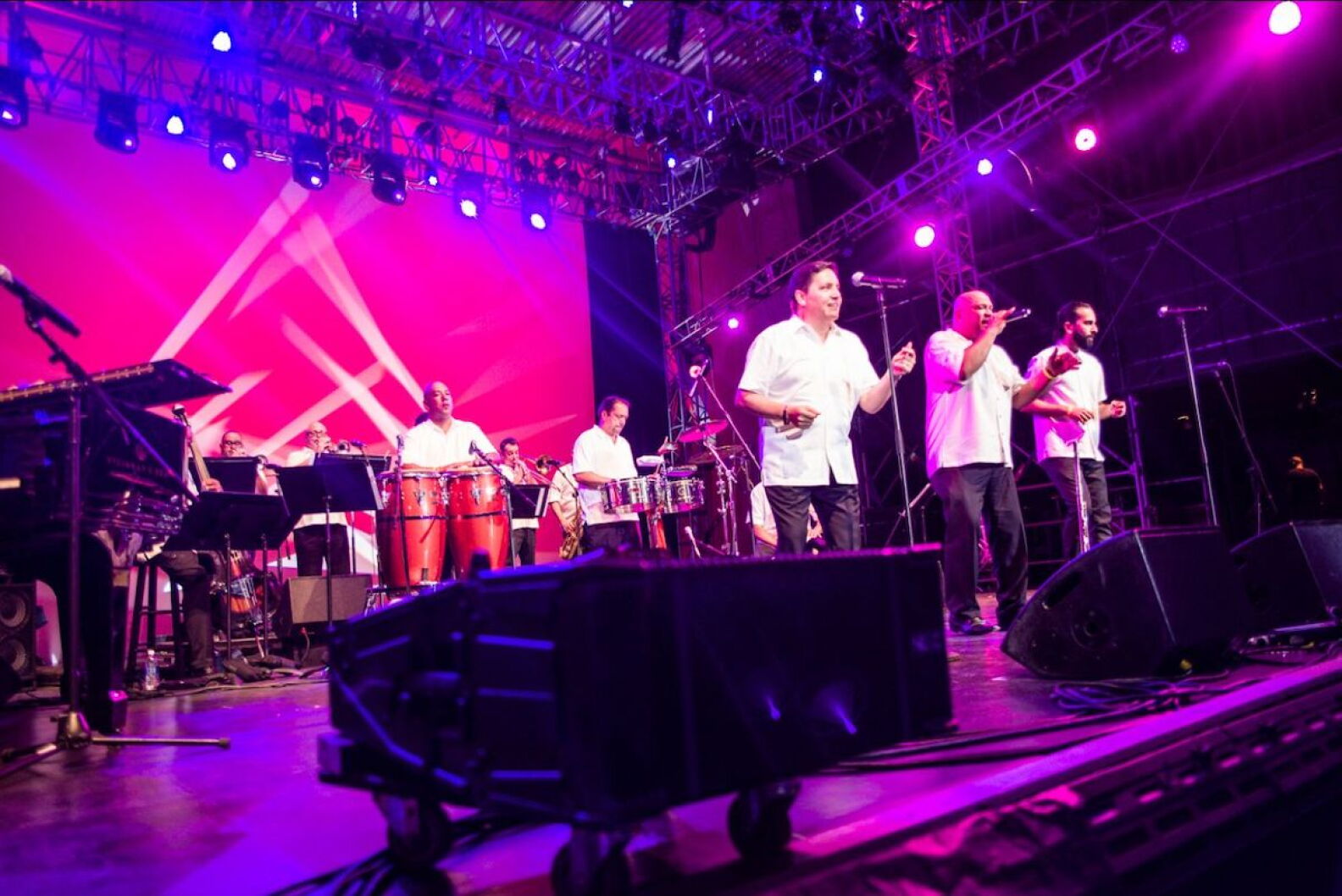 Performers wearing white sing on stage in front of a live band.