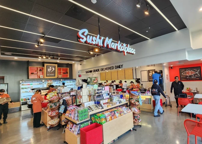 A wide shot of a grocery store's interior where a sign reading "Sushi Marketplace" hangs from the ceiling. 
