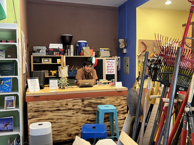 Lending library manager César Montero sits at the front desk of the library surrounded by items that can be checked out.
