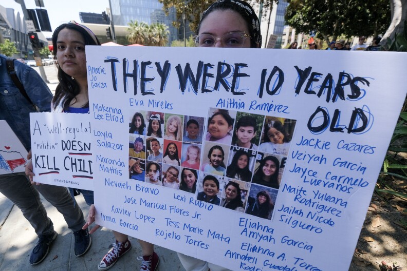 A person carries a homemade posters with the images and faces of the Uvalde school shooting victims with the words "They were 10 years old" in all caps.