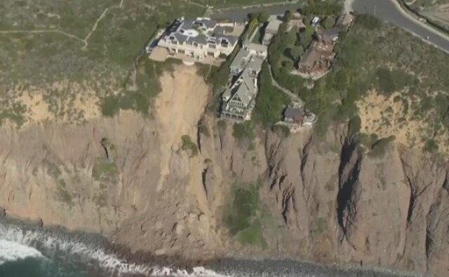An aerial view shows a large mansion perched on the edge of an eroding seaside cliff