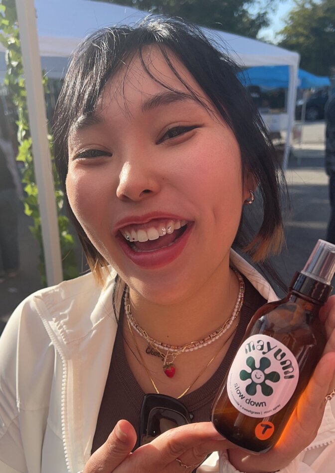 A young Asian woman holding up a bottle that says "Mayumi Slow Down"