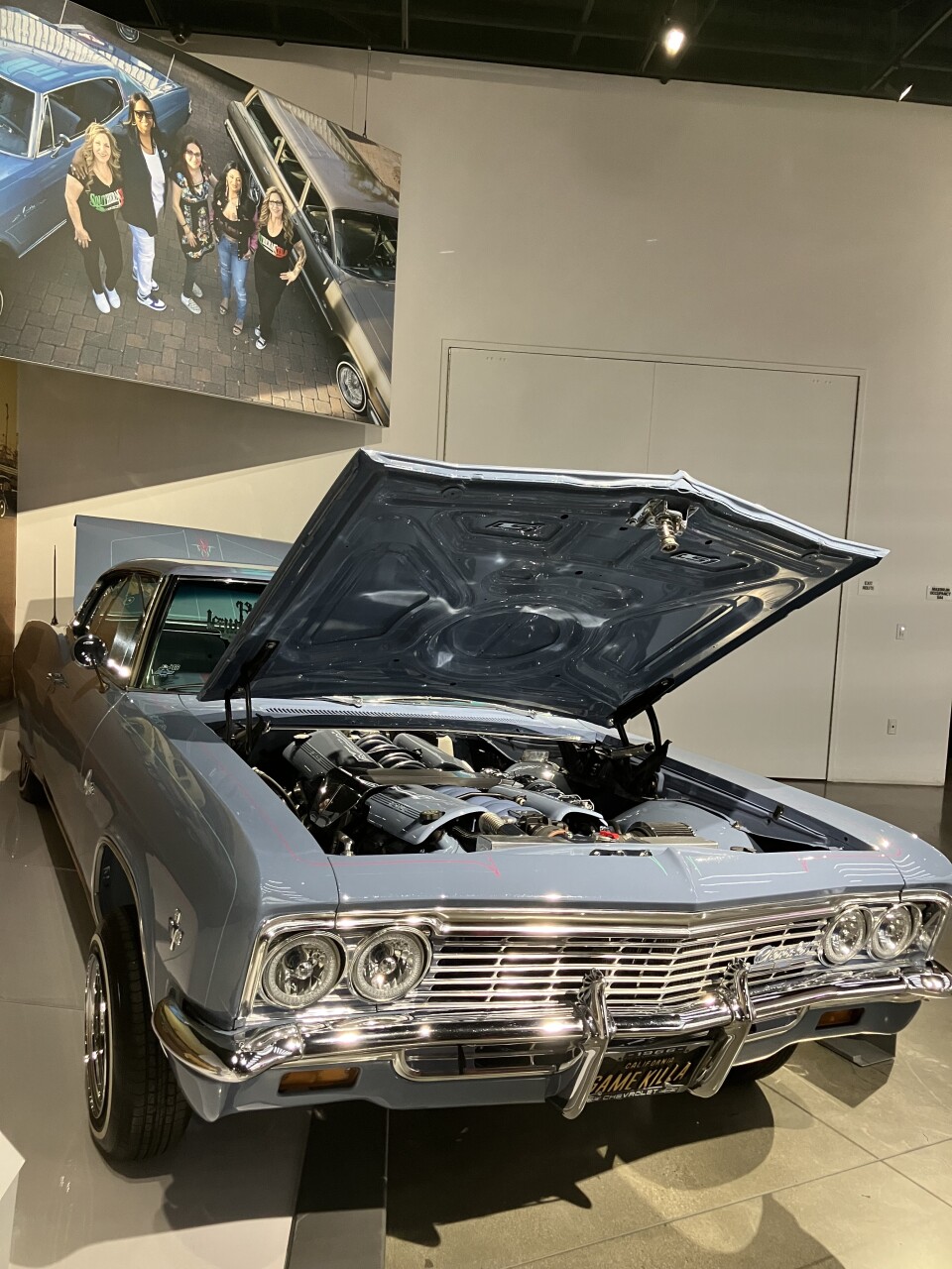 A baby blue classic car with a chrome grill is displayed with its hood open.