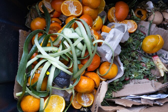 A black tote full of food waste, including cucumbers, citrus and strawberry tops.