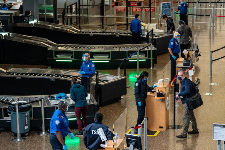 Security area at an airport has TSA officers and people standing at desks.