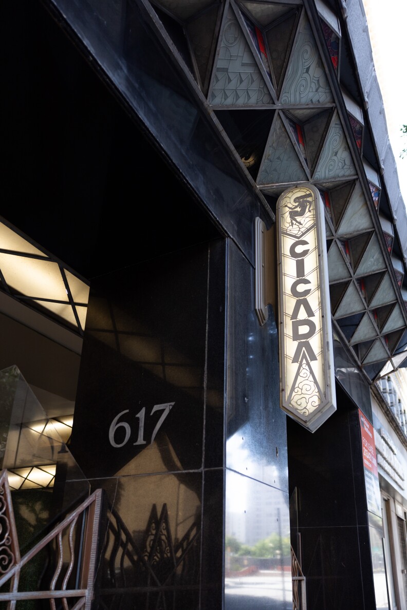 A close up of an art deco lit up sign that reads "CICADA"