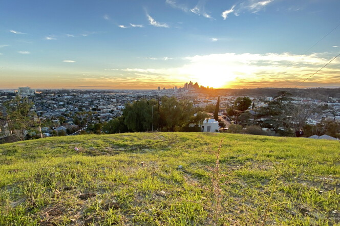 A wide view from the grassy hilltop at sunset. The cityscape of downtown Los Angeles is viewable in the distance.