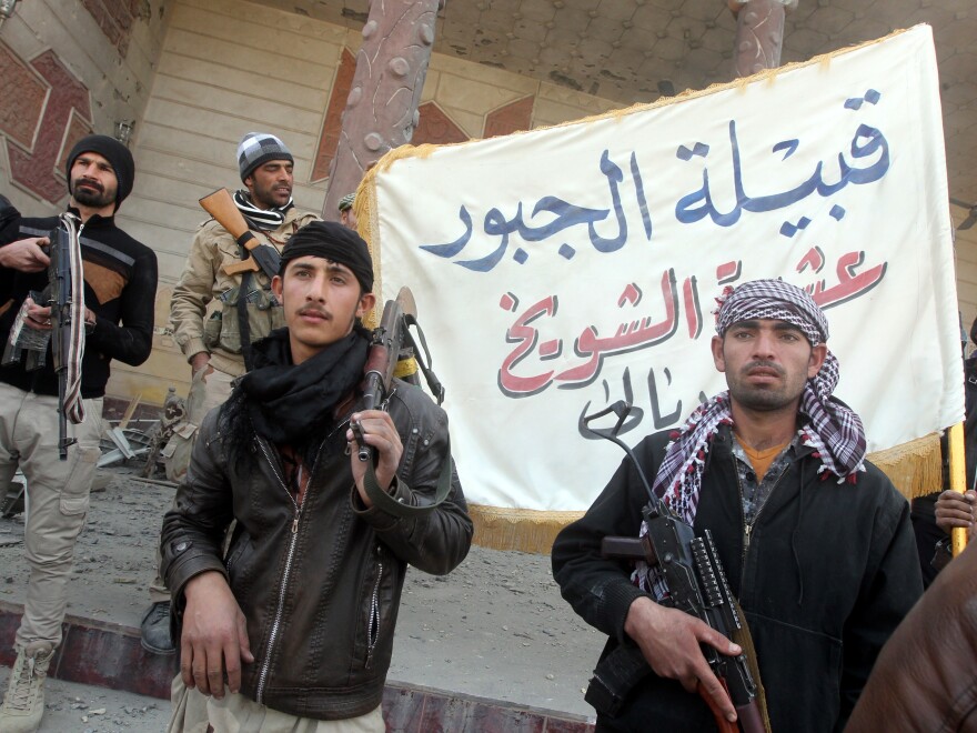 Iraqi Sunni fighters from the Jubur tribe hold a flag in front of a house damaged during clashes with the Islamic State in the village of Sharween, northeast of Baghdad, on Jan. 27. The U.S. is trying to get more Sunni tribes to drop their support for ISIS and fight with the Iraqi government and the Americans.