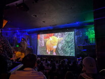 A group of people in a theater watching a film about an animated cow.