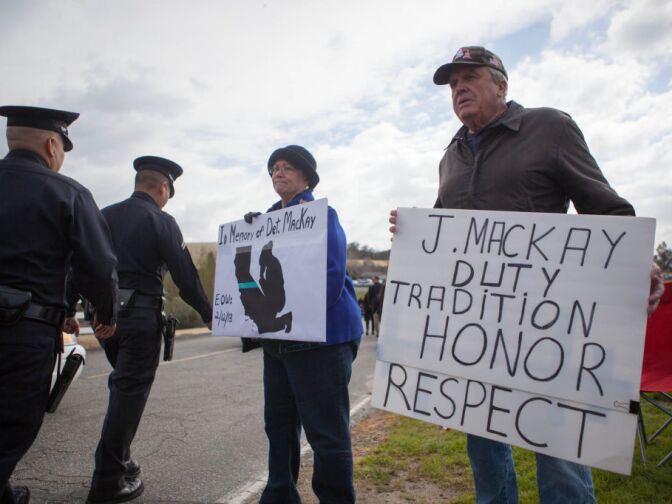 Vaughn Becht of Westminster and Adrienne Murphy of Tustin hold signs as officers walk to the funeral for Det. Jeremiah MacKay in San Bernardino on Feb. 21, 2013.
