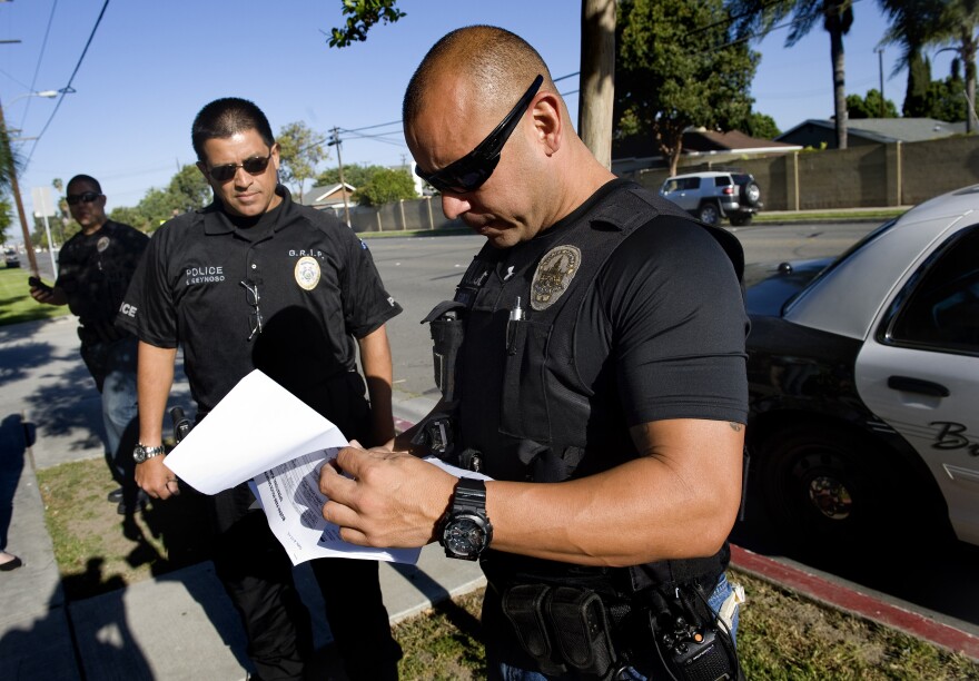 Buena Park police officer James Woo, left, Orange County District Attorney investigator Francisco Reynoso, center, and Buena Park police officer Luis Garcia look over their paperwork before approaching a Buena Park resident who was arrested in a truancy sweep Thursday morning.