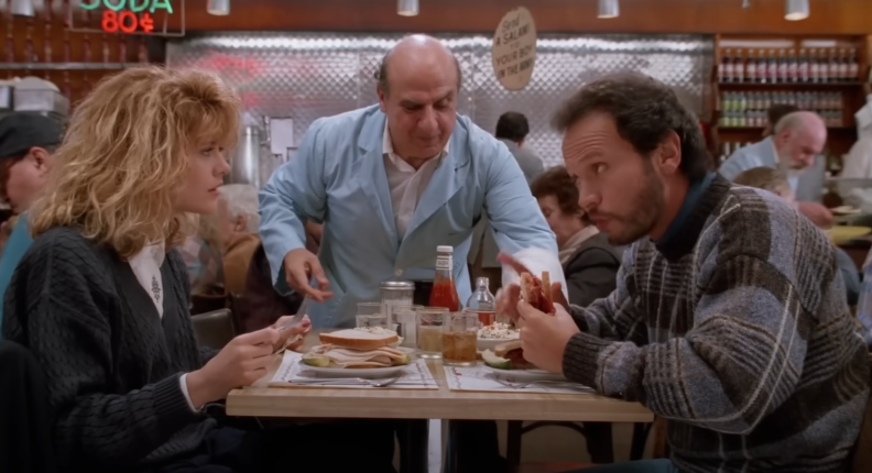 Two people sit at a diner table enjoying deli sandwiches and are deep in conversation.