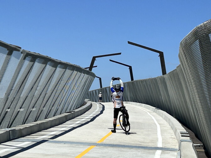 A cyclist in full gear taking a picture of the new bridge he is on.