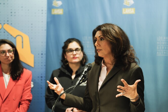 A woman speaks at a podium as two women look on from behind.