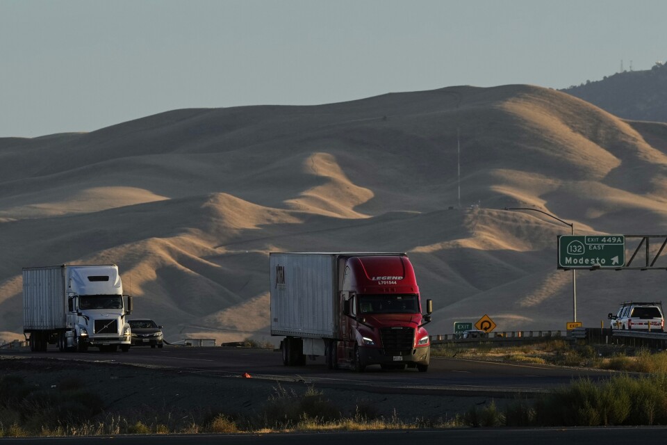 Large trucks are driving along a road surrounded by large hills.