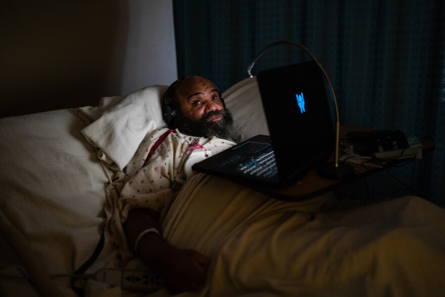 A man laying in bed with headphones and a laptop resting on his belly