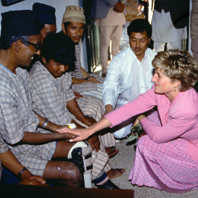 princess diana wearing a pink dress kneels to touch hands with a man