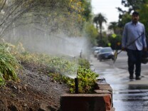 A gardener walks past a row of sprinklers watering plants and foliage in front of an apartment complex in South Pasadena, California on Jan. 21, 2014. Water is running off the plants and onto the street. This kind of wasteful use of water could soon be permanently banned in California.