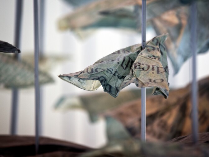 Each paper airplane is hand-folded and clipped onto rods. They reference the Japanese tradition of folding one thousand origami cranes.