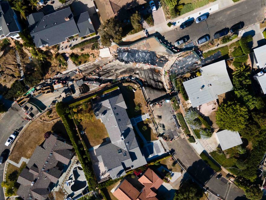 An overhead photo of a curving residential street with broken roads.