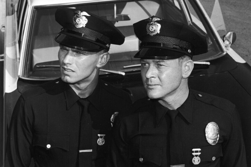 Actors Martin Milner (right) and Kent McCord stand in uniform by their patrol car in a promotional still for the television series, "Adam-12," c. 1969.