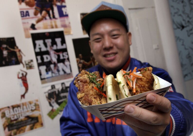 Eddie Huang, co-owner of Baohaus, holds a pair of  "The Taiwanese Te-Bao," a Taiwanese pork chop with curry seasoning, pickles daikon-carrot, jalapeno, aioli and cilantro in a steamed bun, in the New York restaurant, Friday, Feb. 17, 2012.  