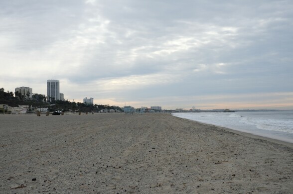 A wide shot looking down a wide sandy beach, with city in the distance. 