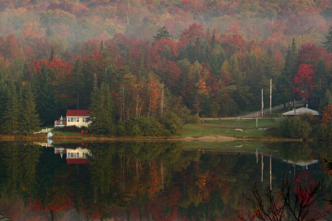 Leaves begin turning color in the early morning mist on October 6, 2007 as houses and trees are reflected on Big Pond near Woodford, Vermont.