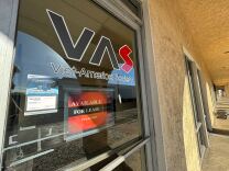 A close-up of a clear glass front door in a long, tan walkway. The door has the text "VAS Viet-America Society" displayed, with an additional sign that says "available for lease" below it.