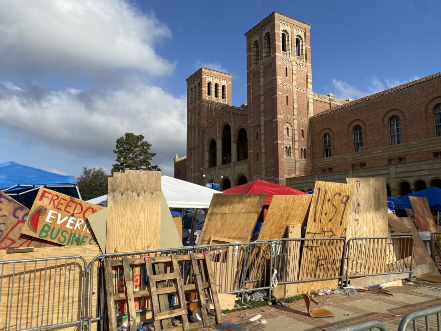 Plywood boards are lined up against metal fencing outside a stately brick building.