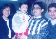 A slightly faded photo of a Latino man with glasses, smiling. holding a little boy with a jacket, red pants and brown hair. He is flanked by a smiling Latina with a bob haircut and a black jacket, and another man with dark hair and a faint mustache. 