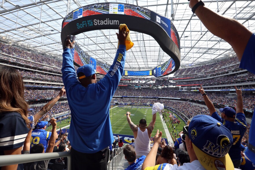 A fan of the Los Angeles Rams stands up with arms raised in reaction to a touchdown by the Rams.