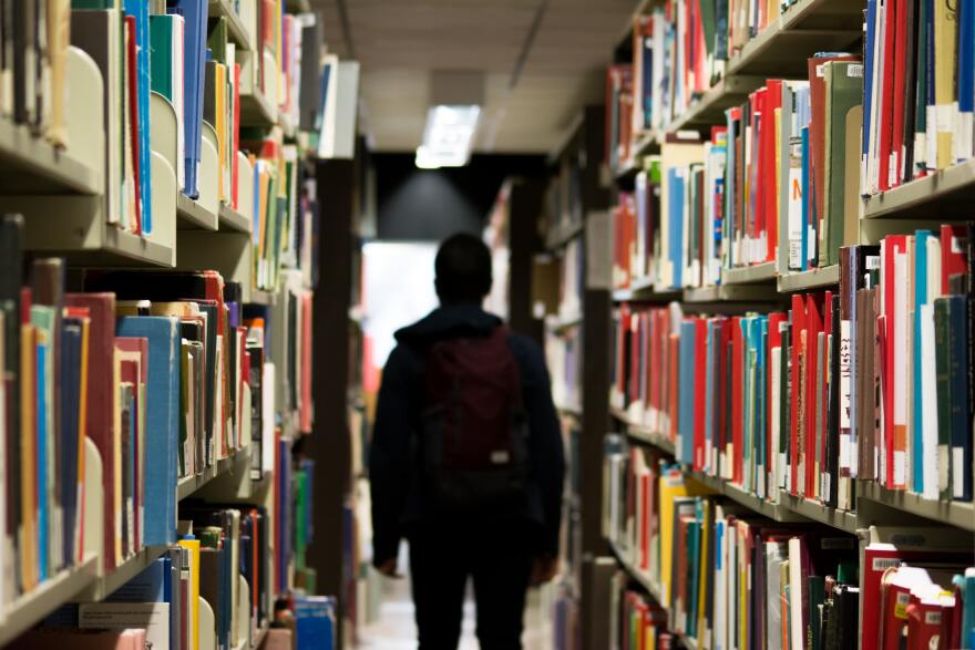 A person wearing a backpack is shown in silhouette in a library.