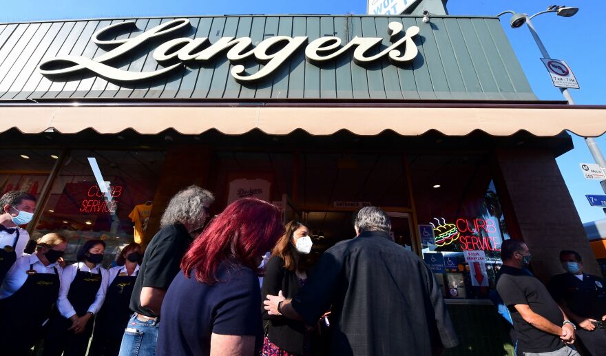 People wearing face masks stand outside a building under a pale green awning that reads Langer's