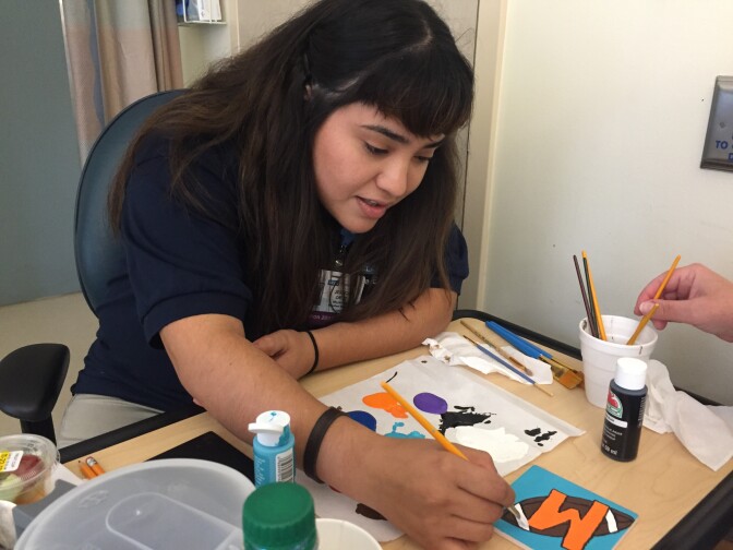 Volunteer Jessica Ortiz helps Rosanna make a coaster. 