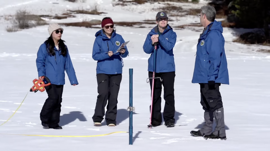 Four people standing on snow with measuring tools.