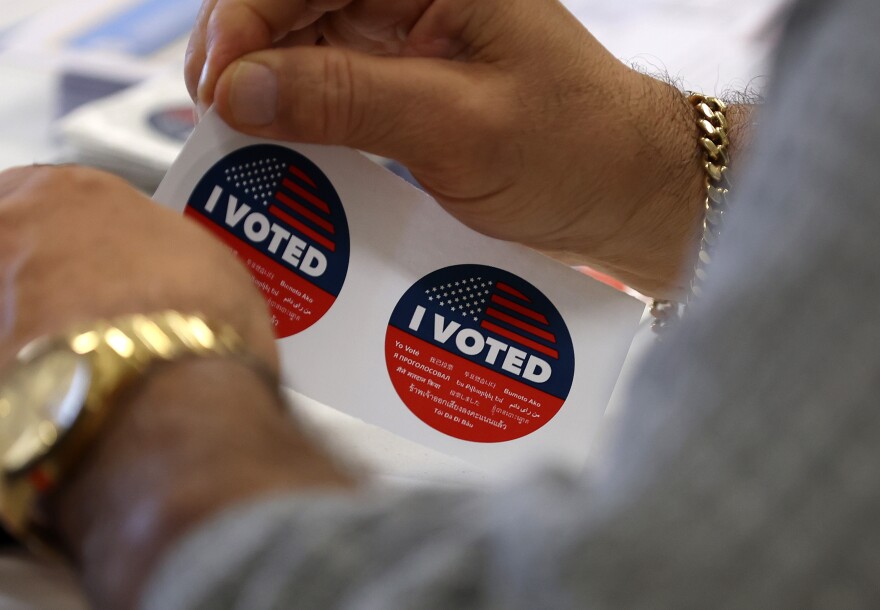A close-up of a pair of hands moving a set of blue, red, and white "I VOTED" stickers on a white sheet.