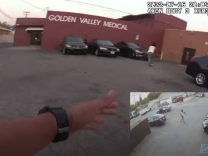 A screenshot from police body-worn camera footage shows Rob Adams turning and running from police in the parking lot of a business in San Bernardino. A police officer's hand is in frame, aiming a gun in Adams direction. 