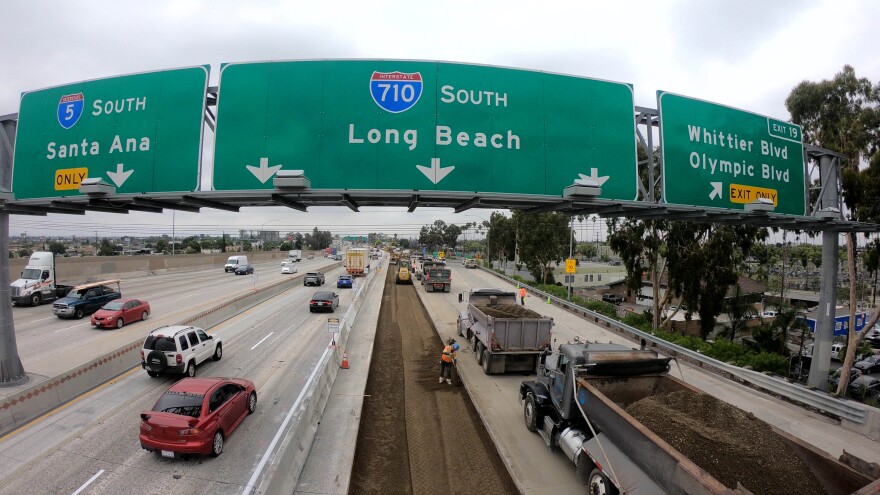 A large green freeway sign indicates lanes for the 5 and 710 freeway. Cars move along lanes on the left as workers repave lanes on the right.