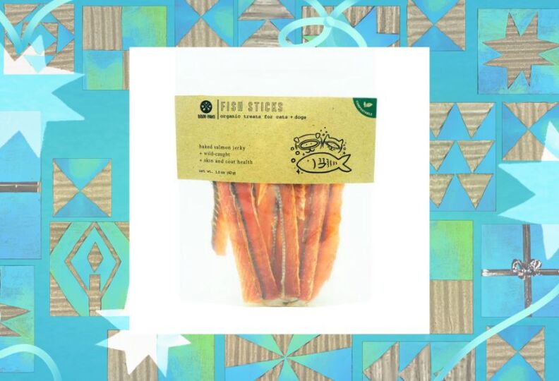 A photograph of a bag of cat treats: The bag is made of clear plastic, and the handle on the bag is a label describing the contents: wild-caught salmon that has been baked and turned into jerky. The contents of the bag kinda look like golden brown French fries, but upon closer inspection the flaky dried layers and textures of the salmon filet strips are visible. The image is set against a decorative teal background accented with stars, gift boxes and strands of ribbon.