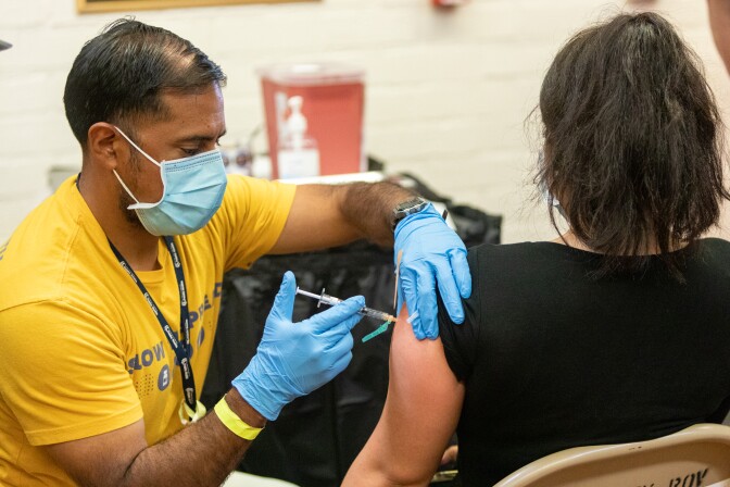 A health care worker in blue gloves and a mask injects a person in their upper arm. 