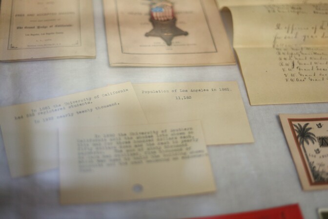 A close up of three small, almost index-sized, tan cards in a display case. The one on the right is in focus, which reads "Population of Los Angeles in 1881: 11,183." Other mementos are around it.